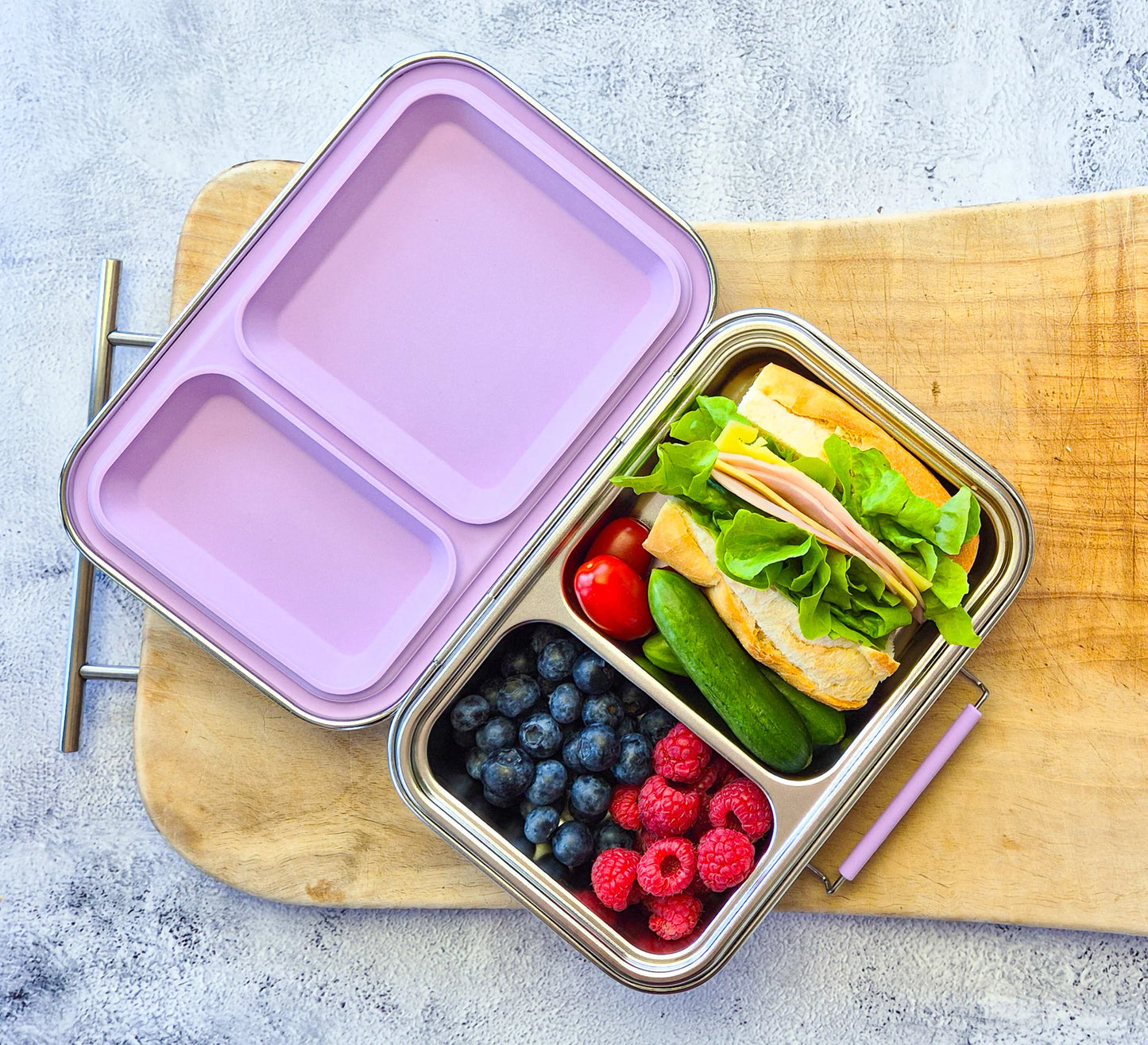 Bento box with a sandwich, fruits, and vegetables on a wooden board.