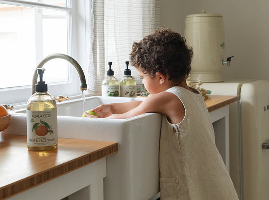 Child washing hands in a kitchen sink with Kool & Co. soap bottles visible.