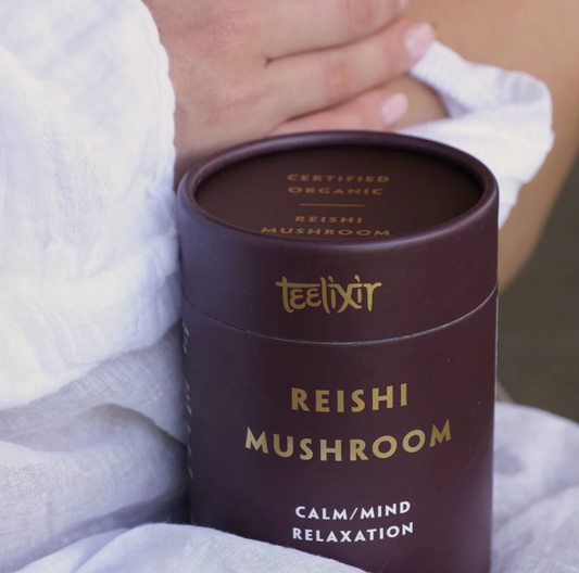 Teelixir Reishi Mushroom product packaging held by a person in a white robe.
