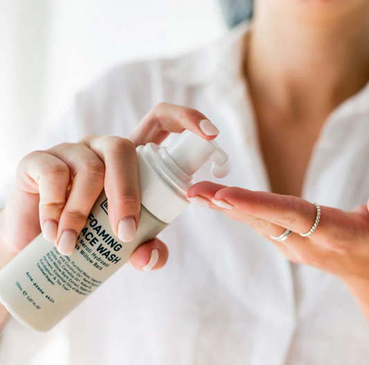 Person holding a bottle of foaming face wash with a blurred background