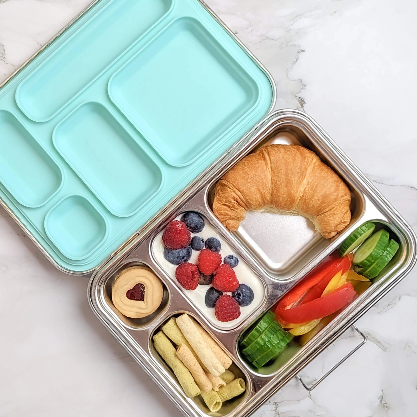 Bento box with compartments filled with a variety of food items on a marble surface